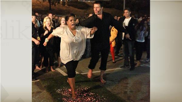 Oprah Winfrey and Tony Robbins walking across hot coals