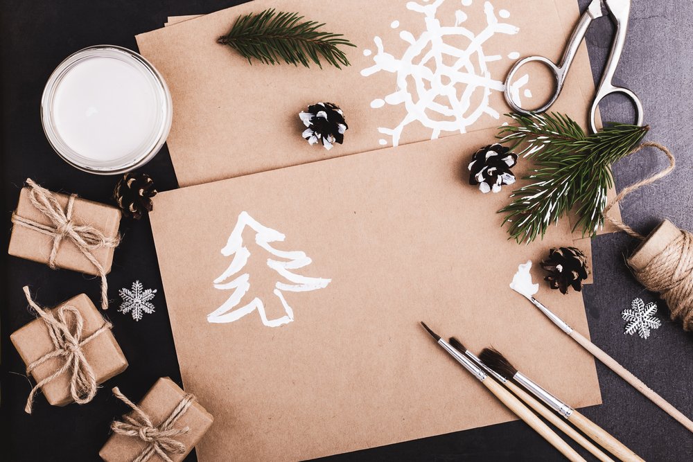 Blank of craft paper, paints and brushes on blue table with copy space for greeting text viewed from above, Christmas holiday theme