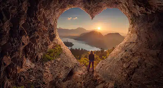 Young woman in heart shape cave towards the idyllic sunrise-awaken