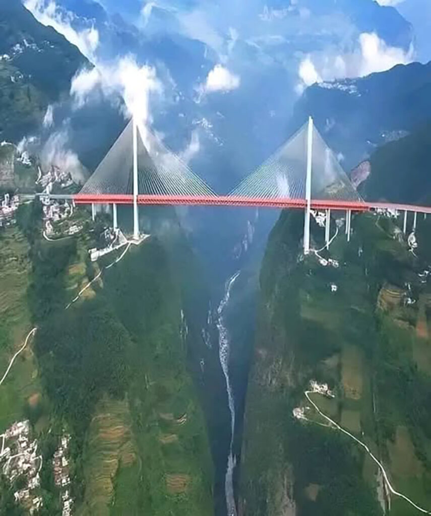 A giant suspended between mountains, the Duge Bridge is one of the marvels of modern engineering. Towering 565 meters above the Beipan River, it is the highest cable-stayed bridge in the world, connecting China's Guizhou and Yunnan provinces. Its sleek red structure spans 1,340 meters, defying the abyss and drastically reducing travel time in this mountainous region.-awaken